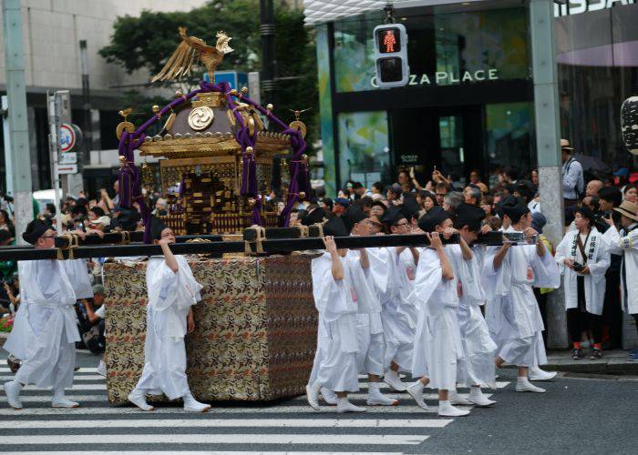 The elegant shrine of Sanno Matsuri in Tokyo, being carried by men in white as onlookers take pictures.